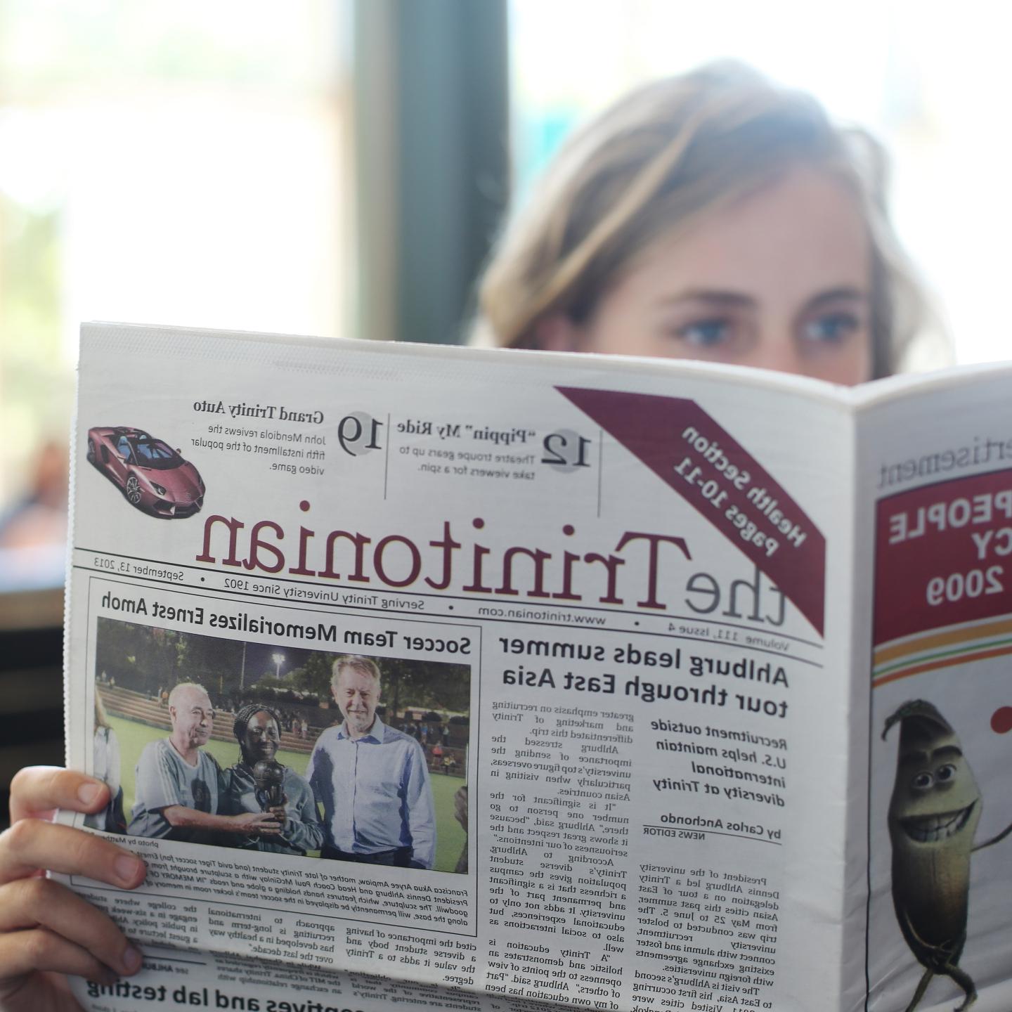 a woman reads a Trinitonian newspaper from 2013